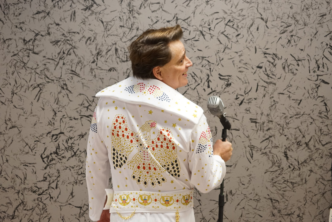 An actor posing as elvis presely for the elvis play, wearing the iconic white jacket with a bejeweled eagle on the back holding the mic